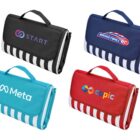 Four rectangular striped picnic blankets with carrying handles are displayed. They are folded and come in black, blue, and red, each featuring a different logo or brand name. The logos are START, Basketball, Meta, and copic.