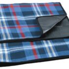 A folded picnic blanket with a blue, red, and white plaid pattern. The underside is black and appears waterproof.