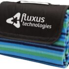 A folded picnic blanket with a blue, green, and black striped design. The flap features the Fluxus Technologies logo in white.