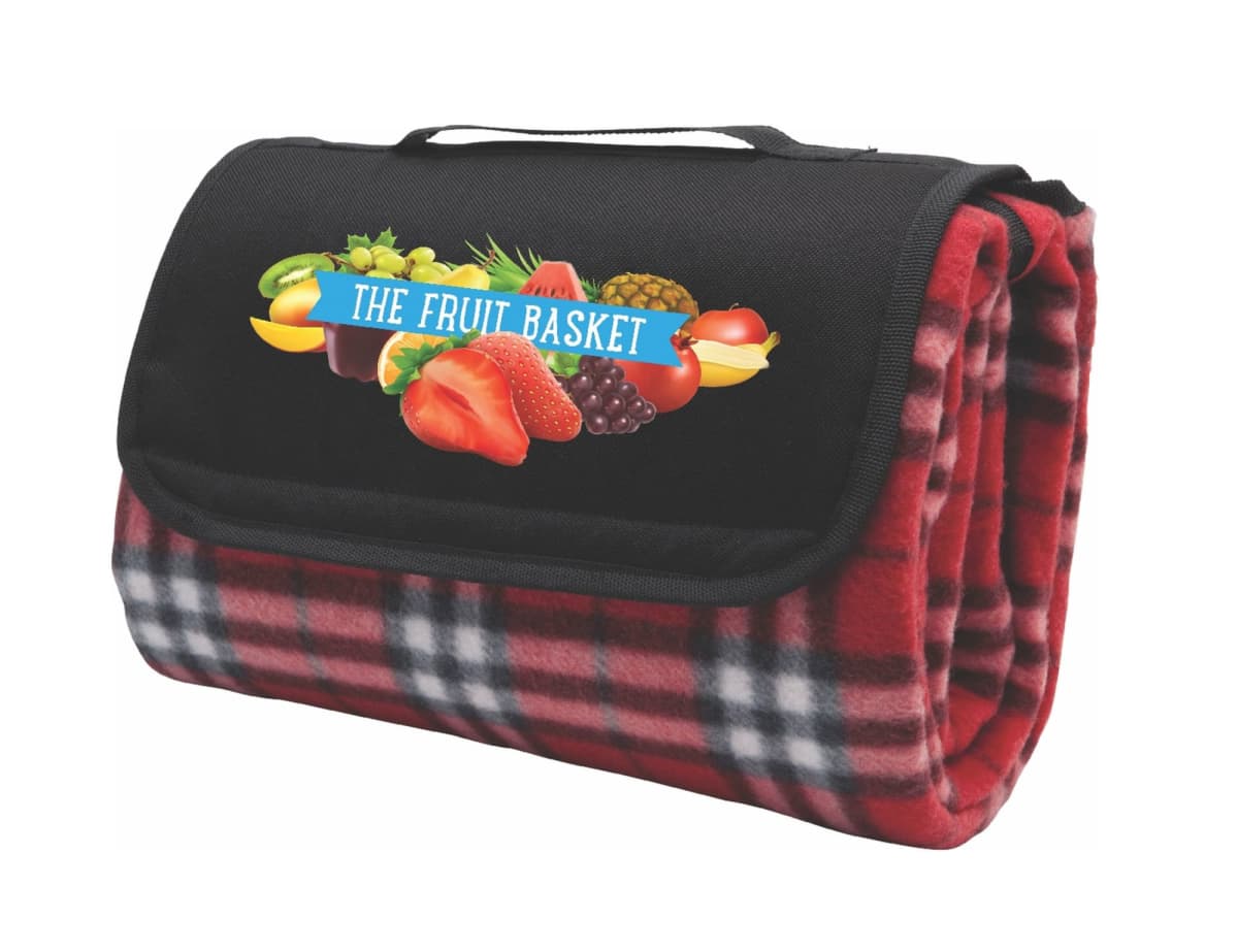 A folded red and black plaid blanket with a black flap featuring a logo for The Fruit Basket, decorated with images of various fruits. The blanket has a handle on top for easy carrying.