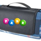 A folded blue plaid picnic blanket with a black carrying handle. The blanket has colorful letters spelling PARK on the front flap.