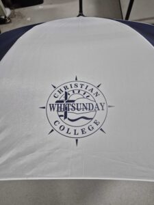 White and navy golf umbrella printed with the Christian Whitsunday College logo in navy on the canopy.
