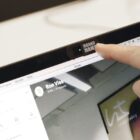 Finger sliding a webcam cover on a laptop screen during a video call.