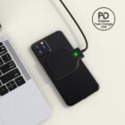 Smartphone with wireless charger pad beside a laptop on a light surface.