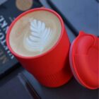 Red cup with latte art next to its lid, on a table.