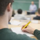 Student taking notes with Memo Pens (Our Best Seller), teacher blurred in the background.