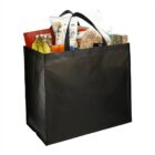 Black reusable shopping bag filled with groceries like bananas, bread, and snacks.