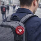 Person wearing a backpack, The Flasher Badges pin, and holding a coffee cup.