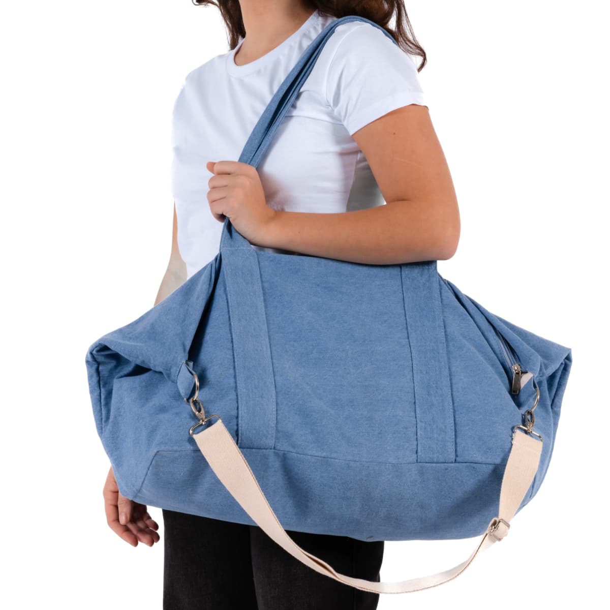 Woman in a white shirt carrying a large blue duffel bag with beige straps.