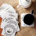 Coasters and a cup of coffee on a table, with a teapot nearby.