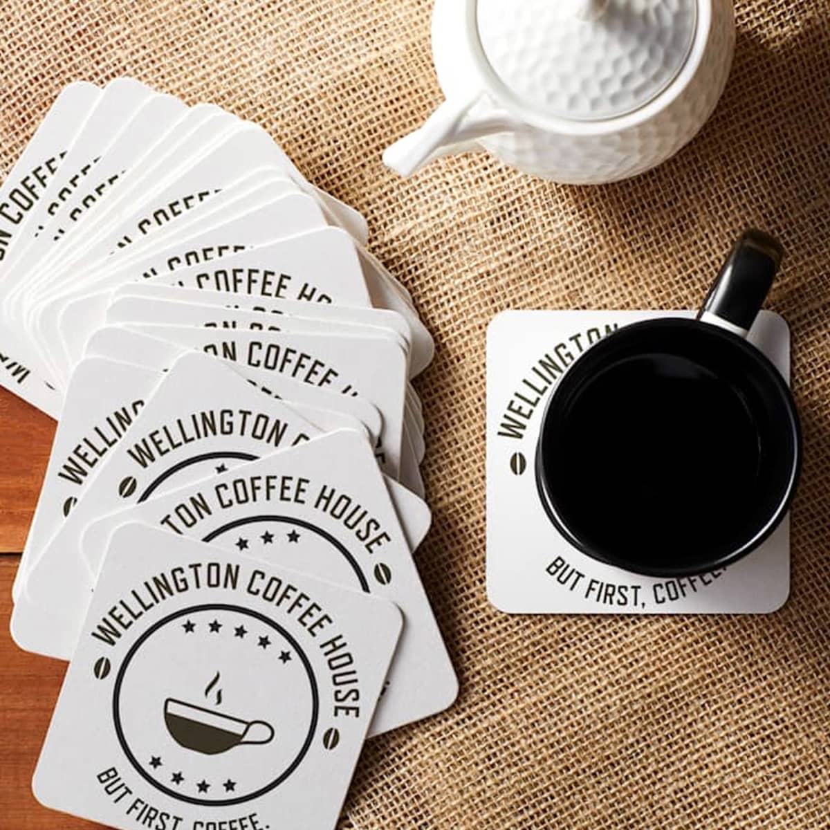 Coasters and a cup of coffee on a table, with a teapot nearby.