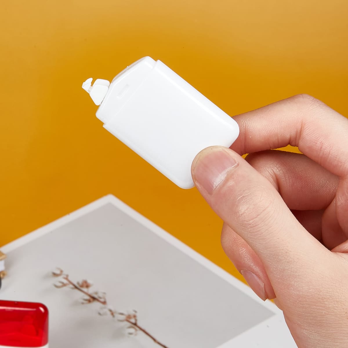 Hand holding a small white rectangular eraser against a mustard background.