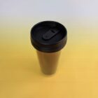 A stainless steel travel tumbler with a black lid on a gradient background transitioning from yellow to light gray.