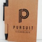 Brown notebook with Pursuit Technology logo, black pen attached on the left side.