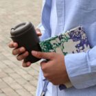 Person holding a travel mug and notebook with a colorful cover.
