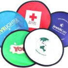 A collection of colorful foldable frisbees with various logos: LiveLighter, Australian Red Cross, Jewish Care, Yogos, and EQFL. Each frisbee is of a different color, such as blue, red, green, and white.