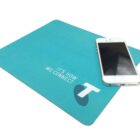 A blue mouse pad with the text Its How We Connect and a stylized T logo. A white smartphone is placed on top of the mouse pad.