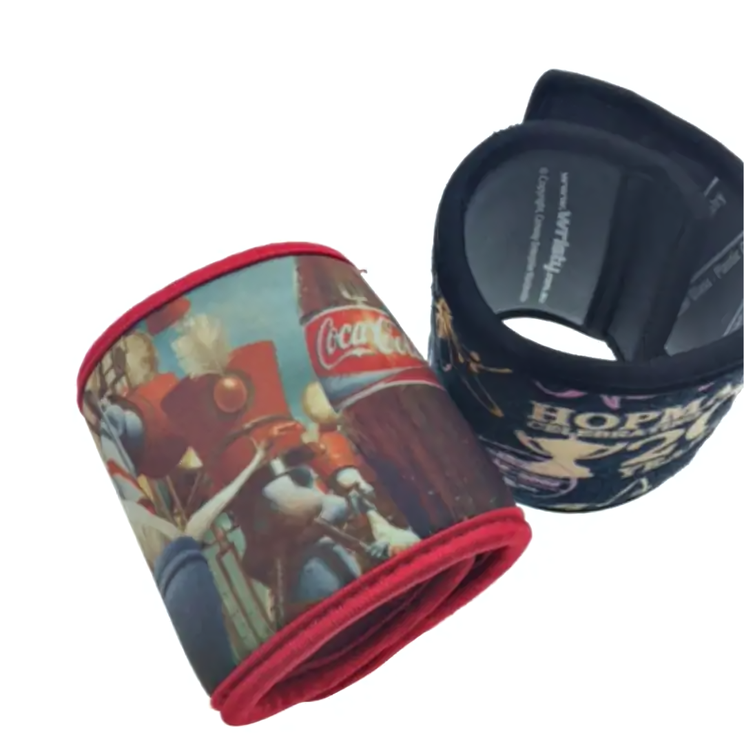 The Stubby Cooler Wrap features two fabric wristbands with vibrant designs: one showcases a Coca-Cola theme with a marching band, while the other boasts Hopkins Live. Both wristbands are rolled up to reveal their colorful patterns and red lining.