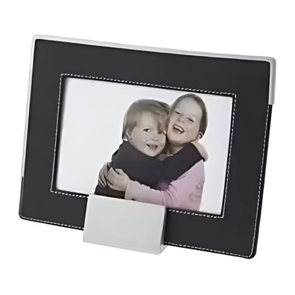 A framed photograph features two smiling children hugging, showcased in the rectangular Troy Picture Frame with a sleek black design, white stitching, and a convenient bottom stand for display.