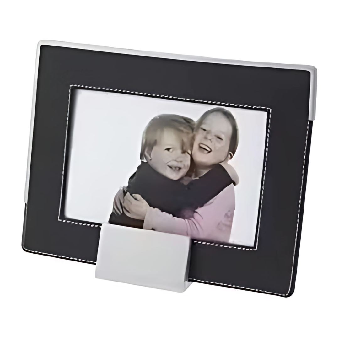 A framed photograph features two smiling children hugging, showcased in the rectangular Troy Picture Frame with a sleek black design, white stitching, and a convenient bottom stand for display.