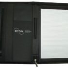 A black zippered leather portfolio is open, showing a lined notepad on the right and a folder with RCSA logo on the left. There are also slots for papers and a pen holder in the middle.