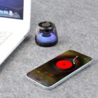 Smartphone with music app, portable speaker, and laptop on a gray surface.