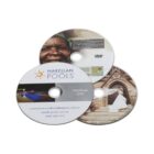 Three DVDs are stacked. The top DVD shows an elderly person smiling. The second DVD reads Narellan Pools Handover DVD and displays a pool image. The bottom DVD features a wedding scene with a couple outside a building. Contact details are visible.