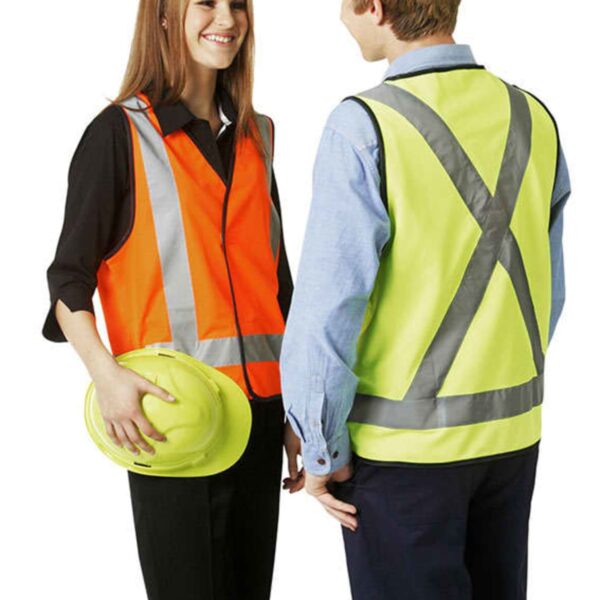 Two people wearing safety vests, one holding a hard hat, standing and talking.