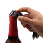 Hand using a keychain bottle opener on a beer bottle with a red cap.