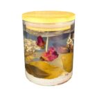 A decorative candle encased in a clear jar with a wooden lid. The candle is embedded with dried flowers and leaves, floating within a translucent, gel-like substance.