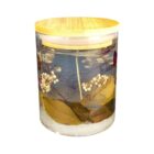 Glass jar with a wooden lid filled with clear water, dried flowers, and leaves. The arrangement appears decorative, showcasing a mix of white blossoms and green foliage submerged inside.