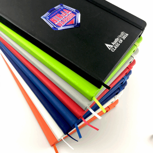 Stack of colorful Rubber feel cover A5 notebooks, top one labeled Ninja Warriors Class of 2016.