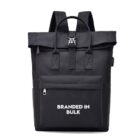 A black backpack features a top handle, shoulder straps, a zippered front pocket, and a clasp closure at the top. The text Branded in Bulk is printed in white on the front pocket.
