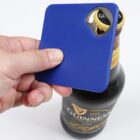 Hand holding a blue card-shaped bottle opener, opening a Guinness bottle.