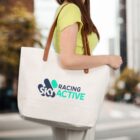 Woman carrying a white tote bag with SKI RACING ACTIVE logo on a city street.