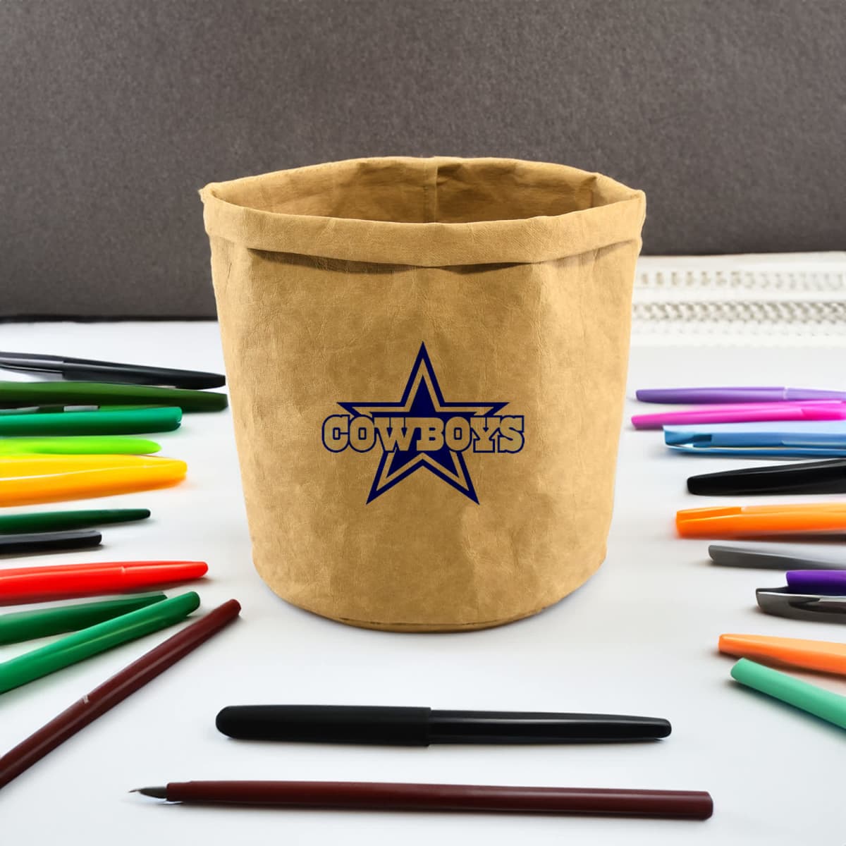 Tan Cowboys-themed pen holder surrounded by colorful pens on a white surface.
