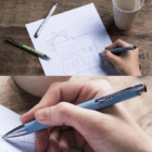 A hand sketches “Going to be Awesome” using Madison Style Eco Pens Promotional on a table.