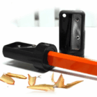 A Promotional Sharpener for Carpenters Pencils sharpens an orange pencil with shavings nearby.