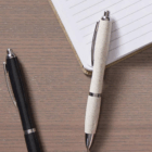 Two Recycled Wheat Stalk Pens Bulk Branded, in black and white, beside a lined notebook.