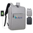 Gray backpack with front pocket and logo reading alyce in blue. Features a USB port for charging, shown with a phone connected. Smaller images show different angles and a black color option.