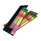 A black cardboard sleeve partially revealing a colorful set of sticky notes arranged like a ruler. The sticky notes are pink, yellow, green, and blue. A wooden backing is visible behind the notes.