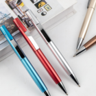 Three Shark Metallic Plastic Pens in blue, red, and silver next to two pens and a closed book.