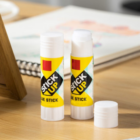 Mini Logo Printed Glue Sticks rest on a wooden table, an open notebook behind.