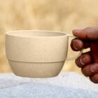 Hand holding a beige cup outdoors with a blurred background.