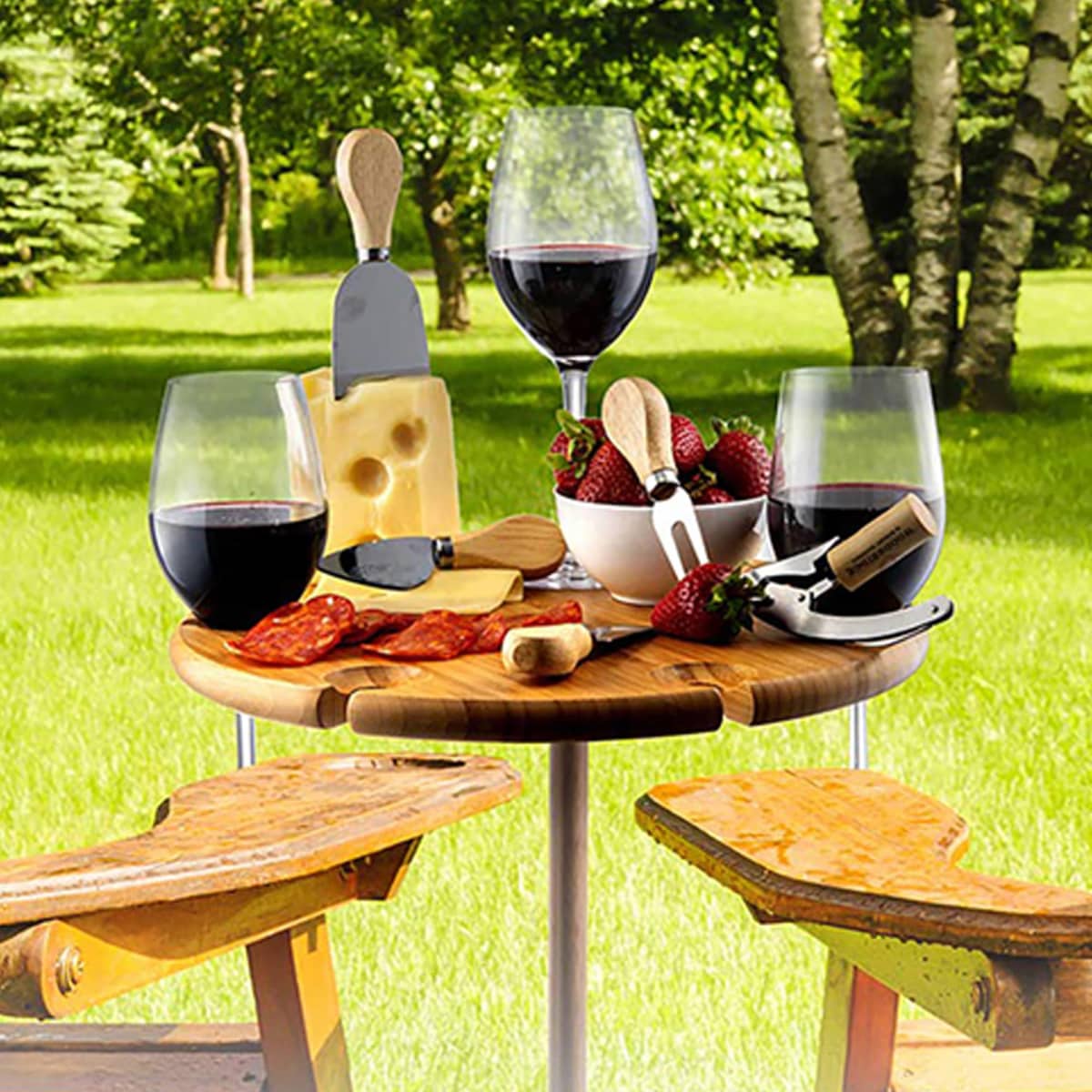 Wine and cheese with strawberries on an outdoor table in a sunny garden setting.