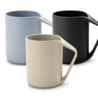 Three minimalist mugs each with a sharp, angular handle are displayed against a white background. They are in light blue, beige, and black colors, and feature a modern, sleek design with smooth surfaces.