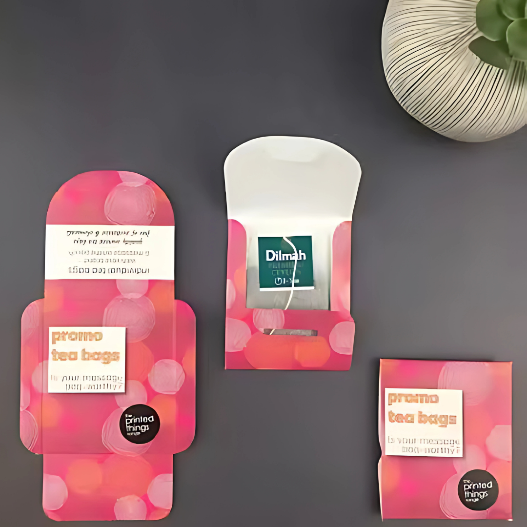Promotional tea bag packets in pink, resting on a sleek gray surface.