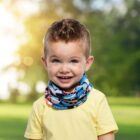 Smiling child in a yellow shirt with a colorful scarf, standing outdoors.