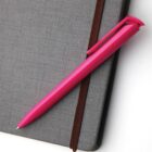 A pink pen rests on a closed gray notebook with an elastic band.