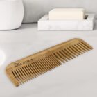 A wooden comb lies on a marble counter near a soap dish and a white container.